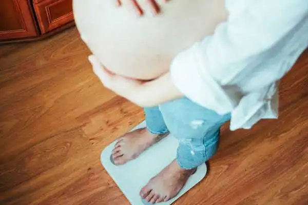 Image of woman weighing herself and experiencing weight gain through pregnancy Seacombe